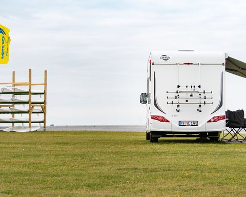 Wohnmobil steht neben einem Regal mit Surfbrettern auf einer Wiese
