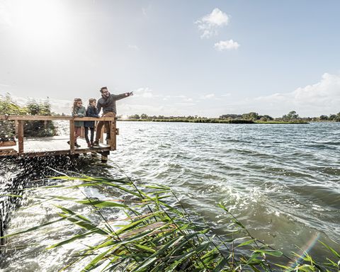 Kleiner Steg an einem See auf dem ein Vater mit zwei Kindern steht. Der Vater zeigt in die Ferne