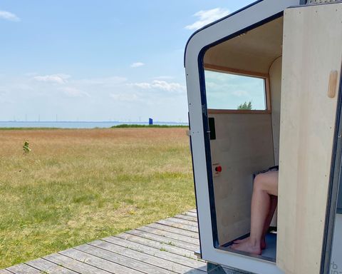 Strandkorbsauna mit offener Tür und Blick auf die Nordsee im Hintergrund. Durch die Tür sieht man die Beine einer Person