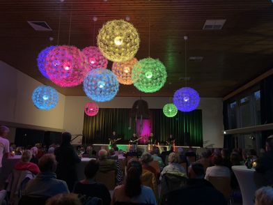 Eine Band spielt vor einem Publikum im Kursaal. Von der Decke hängen große bunte Lampen