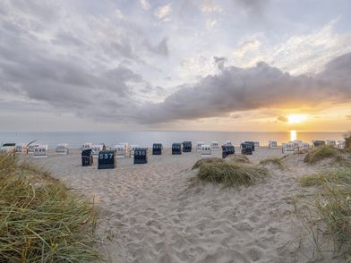 Strand bei Sonnenuntergang mit Strandkörben und Dünen im Vordergrund
