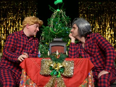 Die Schauspieler Jeffrey von Laun und Vasilios Zavrakis sitzen an einem weihnachtlich gedeckten Tisch und gucken sich an