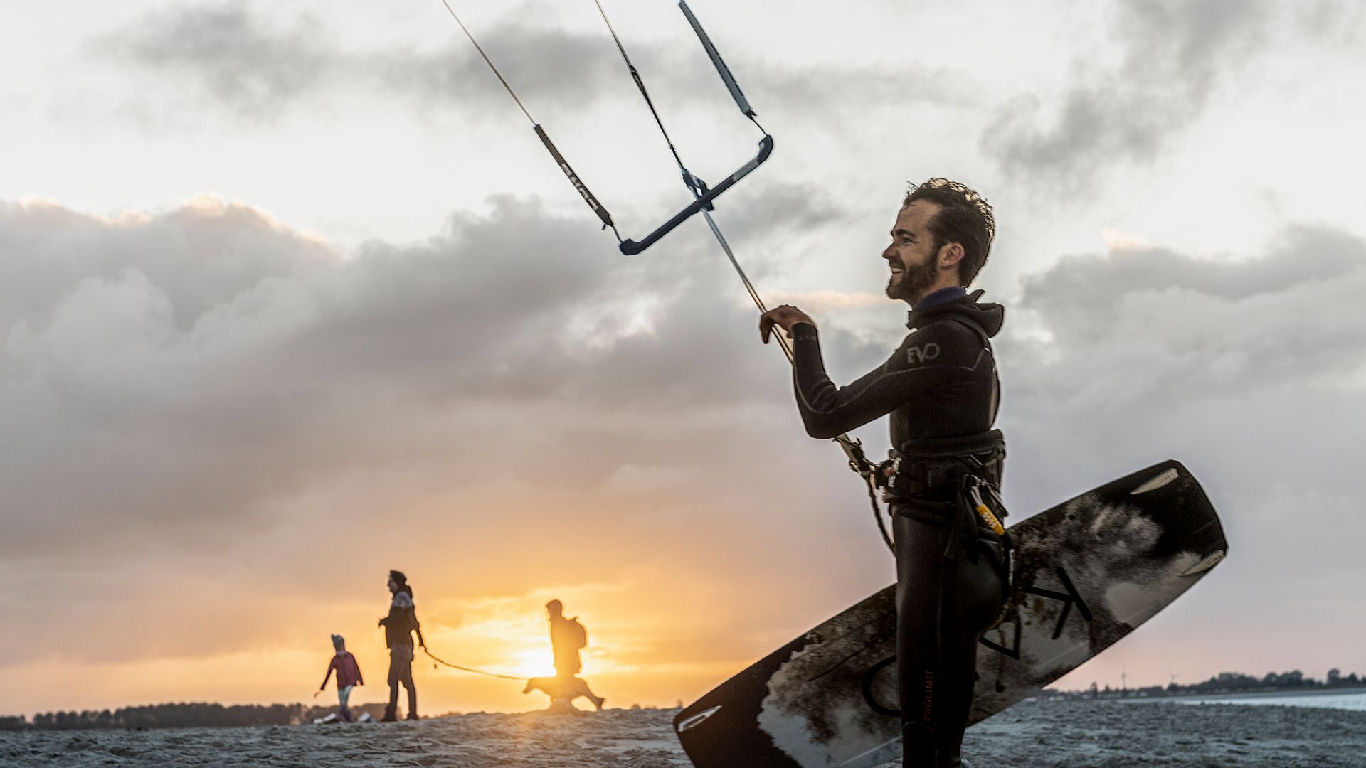 Kitesurfer mit Ausrüstung am Strand bei Sonnenuntergang