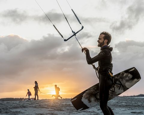 Kitesurfer mit Ausrüstung am Strand bei Sonnenuntergang