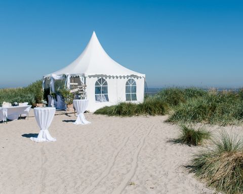 Hochzeitslocation am Strand. weißer Pavillon mit weißen Stehtischen davor