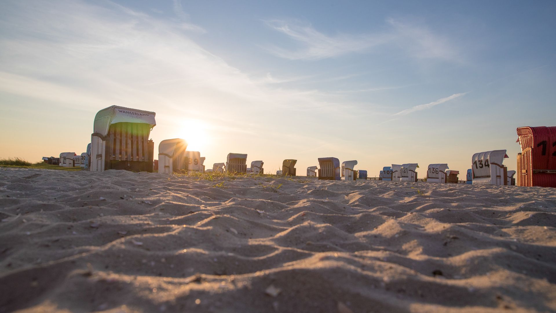 Nahaufnahme von Sand mit Strandkörben und der untergehenden Sonne im Hintergrund