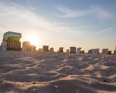 Nahaufnahme von Sand mit Strandkörben und der untergehenden Sonne im Hintergrund