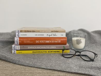 Bücher zum Thema Nachhaltigkeit, eine Kerze und eine Brille auf einer Decke
