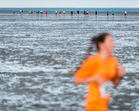 Läuferin im Watt in orangenem Shirt 