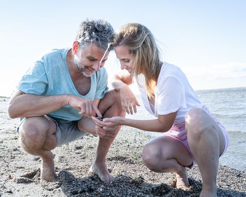 Ein Pärchen hockt am Strand. Die Frau hält etwas in der Hand und der Mann zeigt darauf