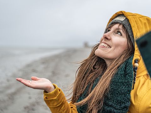 Frau guckt nach oben und hält ihre Hand auf, um zu überprüfen, ob es regnet