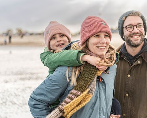 Eine Familie mit einem Kind steht im Watt und guckt in die Ferne. Die Frau hat das Kind auf dem Rücken.