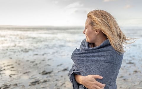 Frau mit Handtuch um den Schultern, die aufs Meer hinausschaut
