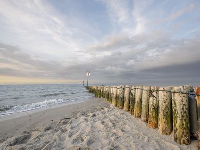 Eine Buhne, die vom Strand ins Meer führt bei Sonnenuntergang